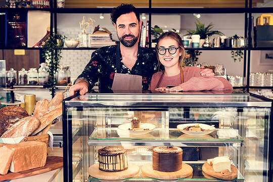 Business owners behind glass cabinet at cafe